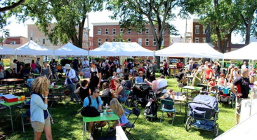 Photo panoramique du marché sur le Parc Durocher : des petits chapiteaux bleus, beaucoup de gens colorés au soleil, vélos, ciel bleu.