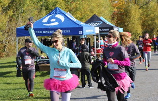 Photo : deux femmes coureuses portent des tutus rose ; plusieurs derrière plus loin ; deux tentes bleues.