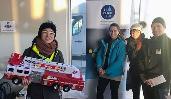 Photo : jeune femme souriante, traits asiatiques, vêtue pour l'hiver, tenant un gros camion de pompiers ; trois autres personnes souriantes sur le côté, deux femmes, un homme. Derrière, affiche Le Pignon Bleu.