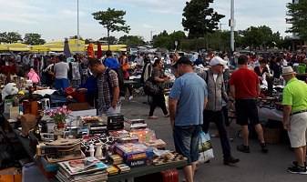 Photo de Marché aux puces de Sainte-Foy, ancêtre de ce nouveau Marché aux puces de Québec. Foule se promenant entre les tables couvertes de livres, appareils, etc. Plusieurs hommes en tenu d'été.